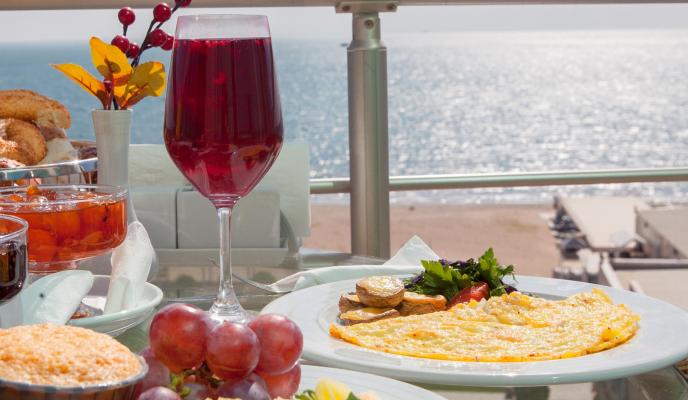 Side view breakfast with baked and grape and omelette in white plate on the balc ony by the sea