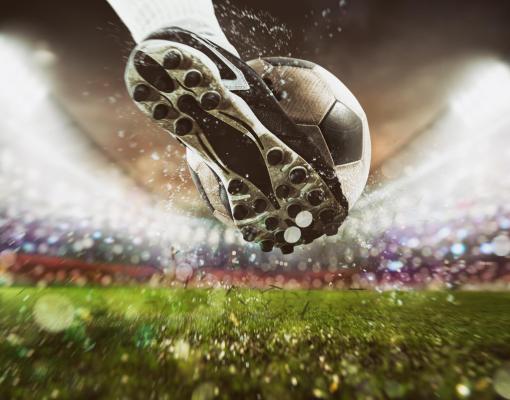 Football scene at night match with close up of a soccer shoe hitting the ball with power